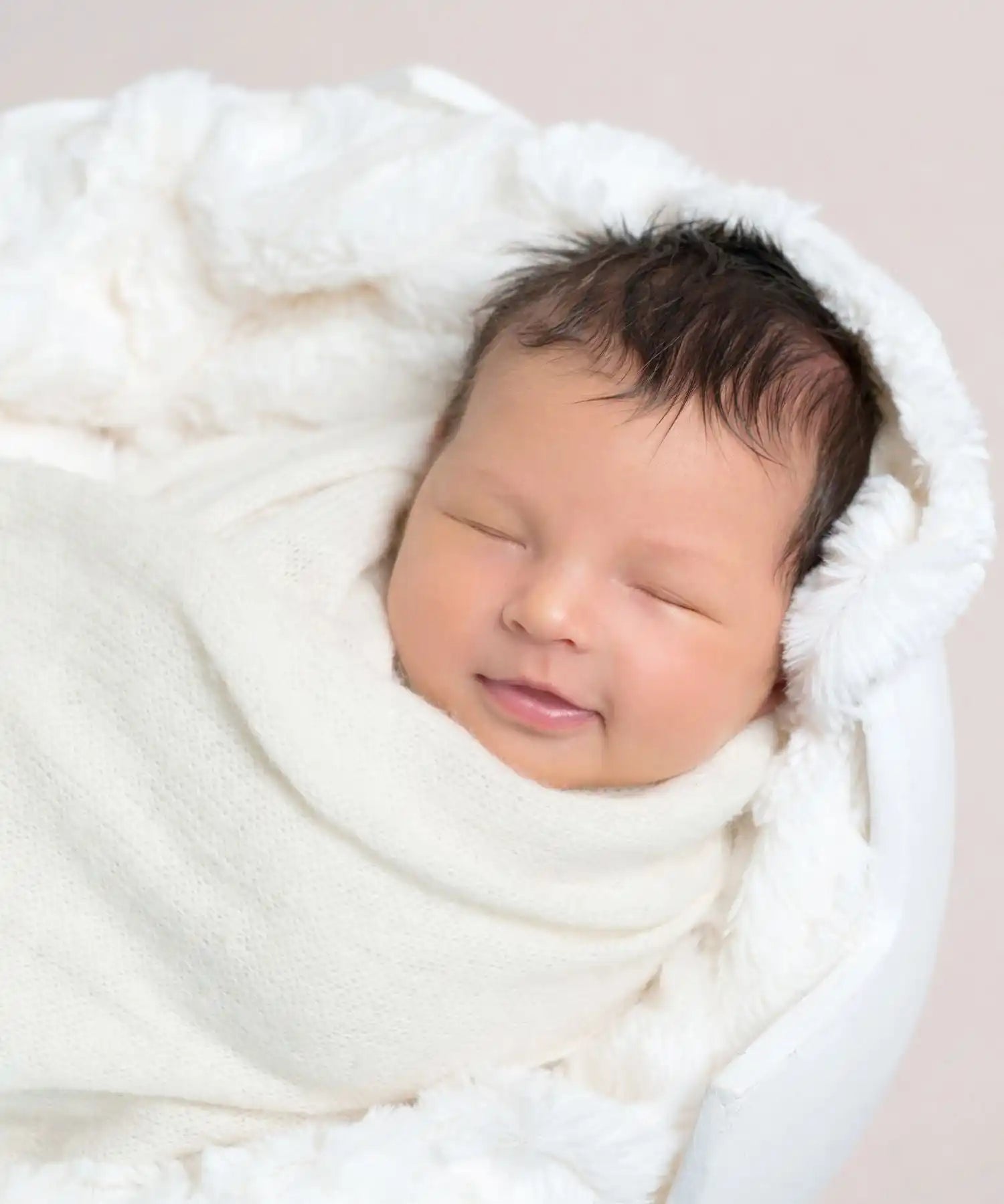 Nouveau-né endormi emmailloté dans du blanc.